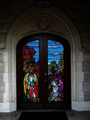 A door to a church is decorated with stained glass panels featuring angels. Make your church shine with stained glass inserts in your entry doors.